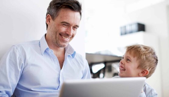 Man using laptop, son watching